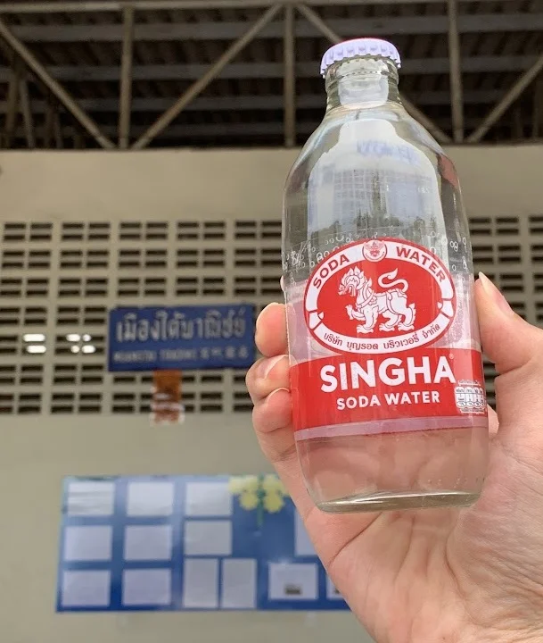 Hands holding soda water with company signed in the background